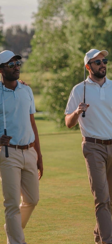 Hombres sonrientes y confiados con gorra y gafas de sol sosteniendo palos de golf y caminando sobre el césped
