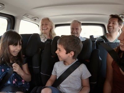 Three generation white family sitting in two rows of passenger seats in a car, looking at each other