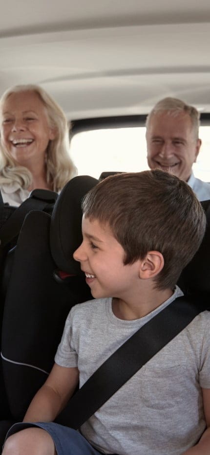 Família branca de três gerações sentada em duas fileiras de assentos de passageiros em um carro, olhando uns para os outros