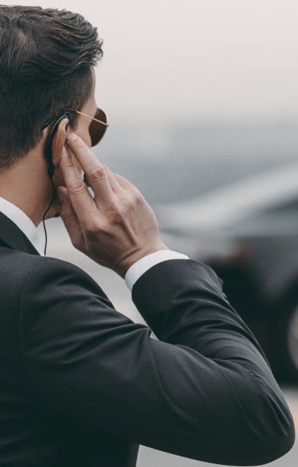 guapo guardaespaldas de pie y escuchando un mensaje con un auricular de seguridad en el helipuerto
