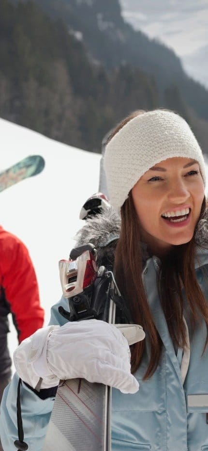 Happy friends carrying skis in snowy field