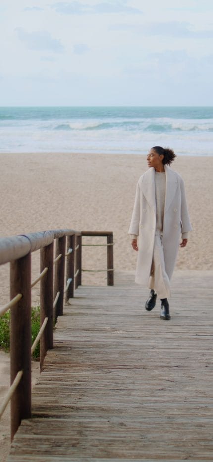 Mulher solitária caminhando pelo caminho de madeira da praia. Sereno afro-americano aproveita o tempo na costa do oceano. Modelo de cabelo preto passeando em um dia nublado. O senhor está em um lugar tranquilo e sozinho.