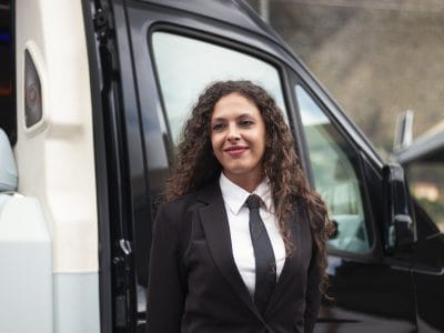 Close up of private chauffeur Concetta from Palermo outside her vehicle looking at camera in a friendly way
