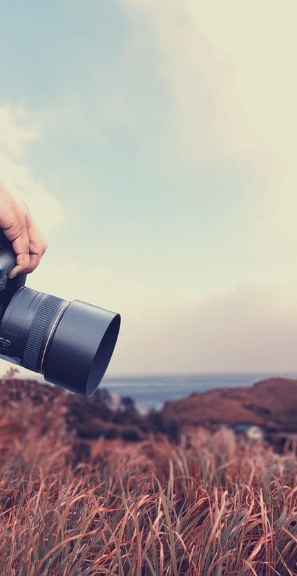 Primer plano de un hombre con una cámara de pie en la colina