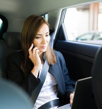 Busy business woman talking on the phone with a coworker while working on a presentation report on her laptop. Businesswoman on her way to work in the back of a taxi cab