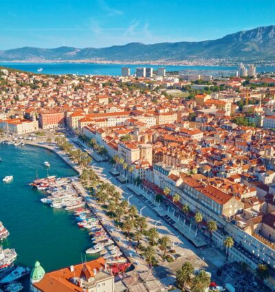 Aerial view of Split, Croatia. Cityscape of a coastal tourist town with a harbor and mountains in the background. Old town with historic red-roofed buildings near the Adriatic Sea.