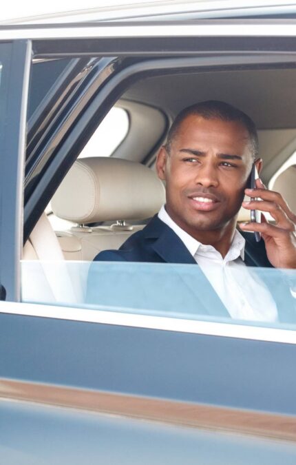 Security guard opening door young businessman sitting in the car talking with friend on smartphone looking aside smiling happy