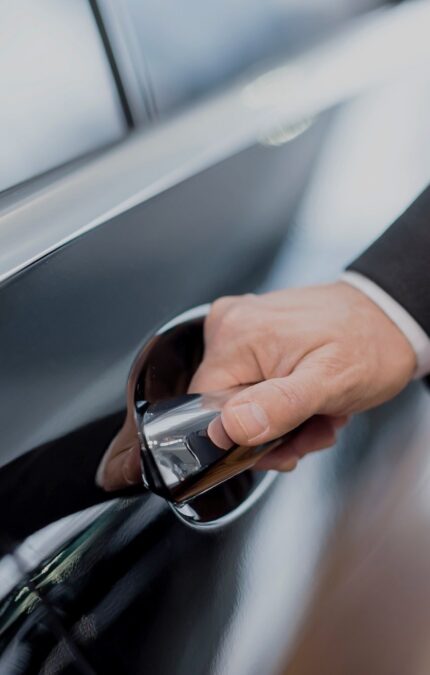 Mano de un chofer uniformado en la acción de abrir la puerta del vehículo.