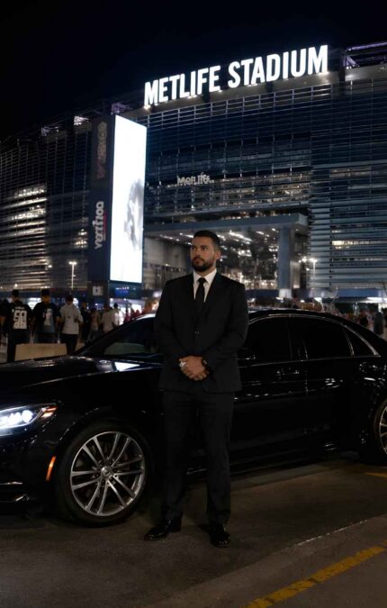 A private driver near MetLife Stadium at night, standing next to his car.
